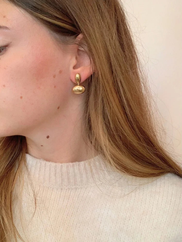 La femme porte les boucles d'oreilles Charlotte dorées en acier inoxydable de chez Au Bonheur de Sophie